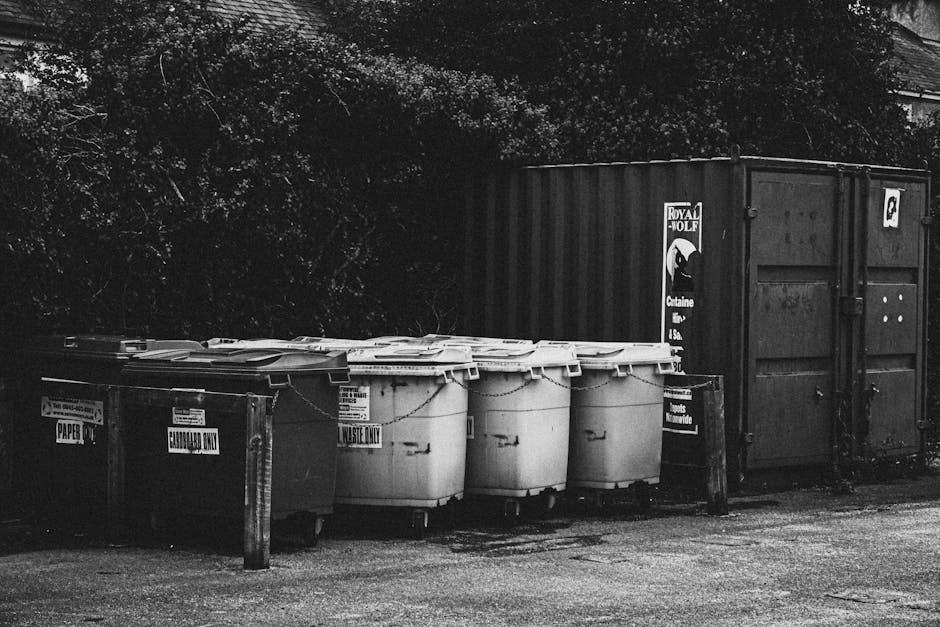 A black wheeled waste disposal bin labeled 'COMMERCIAL WASTE ONLY' is positioned on the pavement in front of a closed restaurant or bar with a rust-red wooden facade and large multi-pane windows. The 