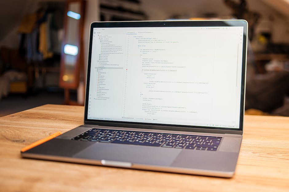 The image shows a modern laptop on a dark surface with a focus on its screen displaying lines of code in a text editor. The code appears to be programming language, possibly JavaScript, with syntax hi